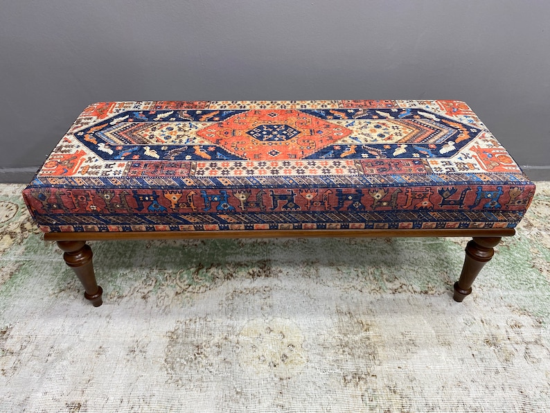 May include: A wooden bench with a colourful patterned cushion. The cushion features a geometric design in shades of red, orange, blue, and white.