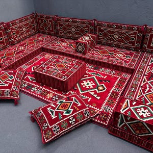May include: A red and white patterned floor seating set with cushions and pillows. The set includes a large rectangular base, smaller square bases, and several cushions and pillows. The cushions and pillows are all decorated with intricate geometric patterns in red, white, and green.