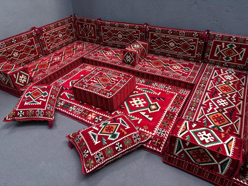 May include: A red and white patterned floor seating set with cushions and pillows. The set includes a large rectangular base, smaller square bases, and several cushions and pillows. The cushions and pillows are all decorated with intricate geometric patterns in red, white, and green.