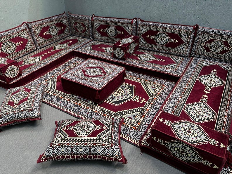 Pu&ograve; includere: Un tradizionale arredamento marocchino con un tappeto, cuscini e cuscini da pavimento a motivi bordeaux e crema. I posti a sedere sono disposti a forma di quadrato con un tavolino al centro.