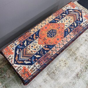 May include: A colourful patterned bench with a blue, orange and white design. The bench is made of fabric and has a rectangular shape.