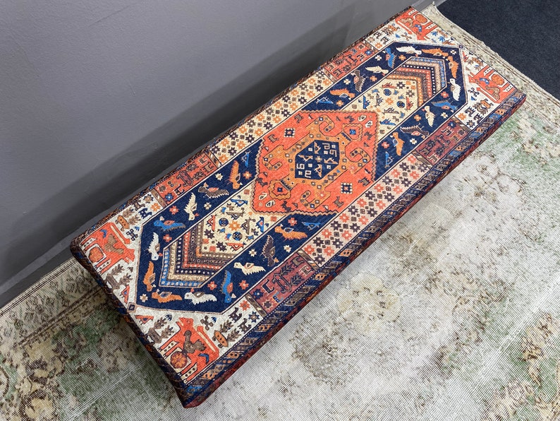 May include: A colourful patterned bench with a blue, orange and white design. The bench is made of fabric and has a rectangular shape.