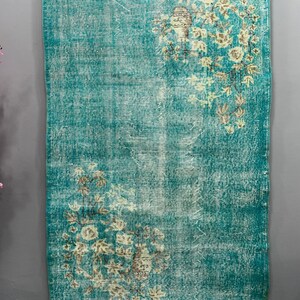 May include: A vintage teal rug with a faded floral pattern. The rug has a distressed look and is made of a soft, woven material.