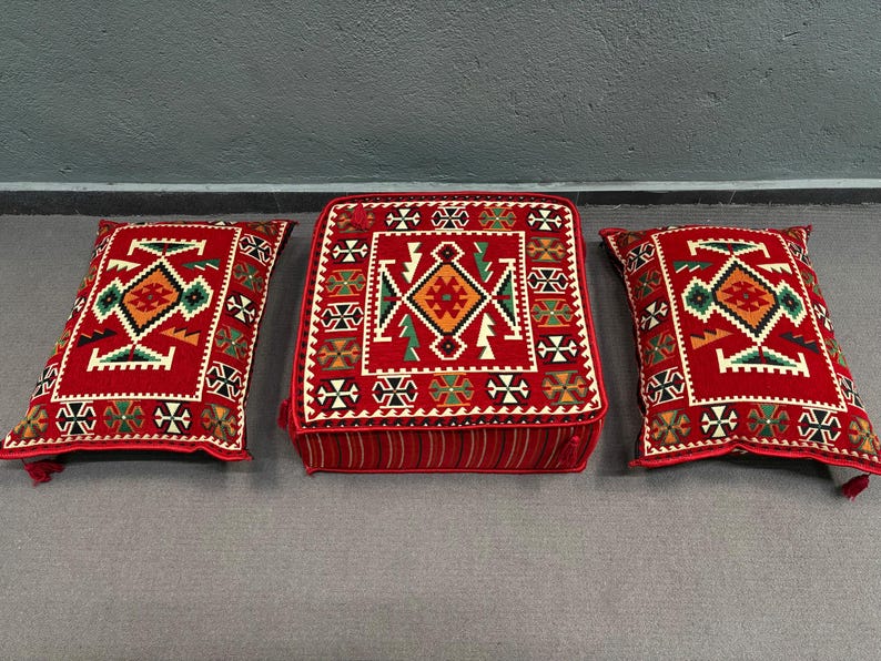 May include: Three red, square cushions with intricate geometric patterns in shades of red, green, and white. The cushions are made of a soft, plush fabric and have a traditional, ethnic design.