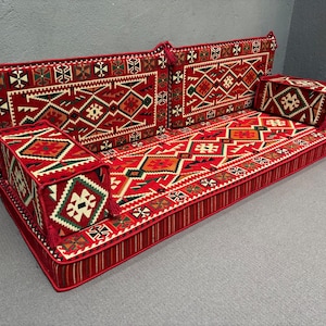 May include: A red and white patterned floor cushion with a geometric design. The cushion is made up of multiple sections and has a tufted border.