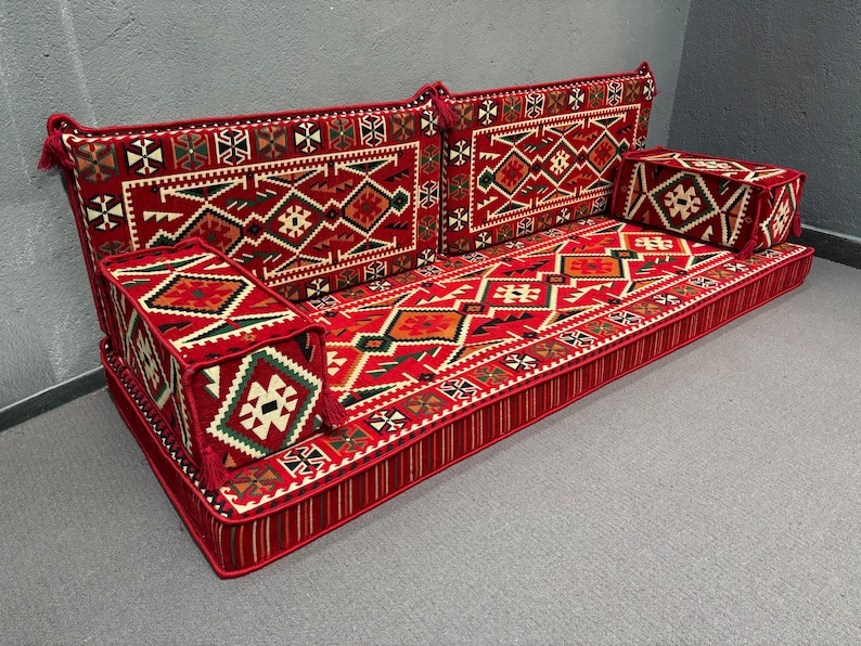 May include: A red and white patterned floor cushion with a geometric design. The cushion is made up of multiple sections and has a tufted border.