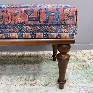 May include: A wooden footstool with turned legs and a colourful patterned fabric top. The fabric features a geometric design with red, blue, and brown colours.
