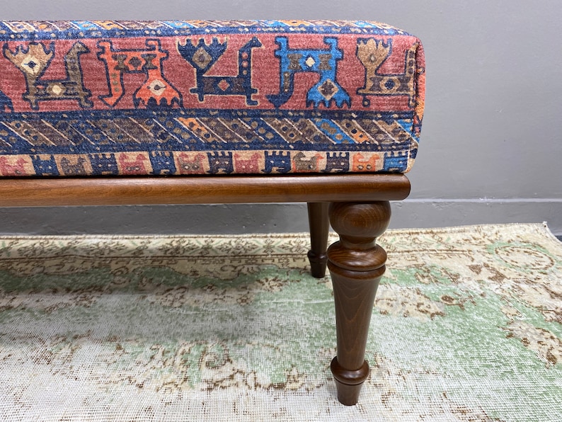 May include: A wooden footstool with turned legs and a colourful patterned fabric top. The fabric features a geometric design with red, blue, and brown colours.