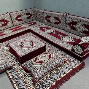 Pu&ograve; includere: Un set di sedute tradizionale marocchino con un tessuto a motivi bordeaux e crema. Il set comprende un grande divano angolare, diversi cuscini pi&ugrave; piccoli e un pouf quadrato. I cuscini e il pouf sono tutti rivestiti dello stesso tessuto del divano.