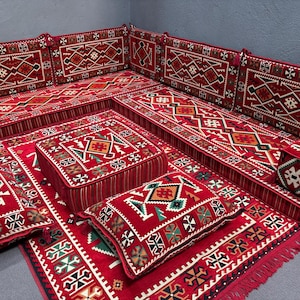 May include: A traditional red and white patterned floor seating set with cushions and pillows. The set includes a large sofa, smaller individual seats, and a square ottoman.