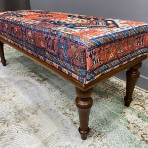 May include: A wooden bench with turned legs and a colourful patterned fabric top. The fabric features a traditional design in shades of red, blue, and brown.