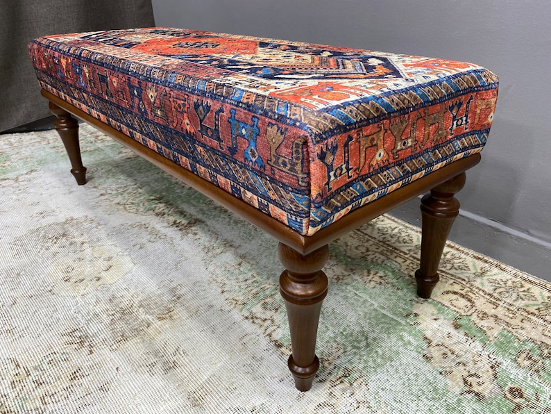 May include: A wooden bench with turned legs and a colourful patterned fabric top. The fabric features a traditional design in shades of red, blue, and brown.