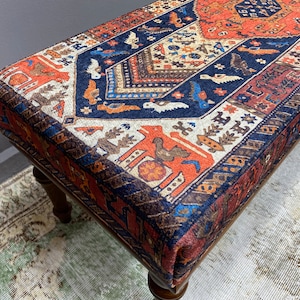 May include: A wooden bench with a colourful patterned cushion. The cushion features a geometric design with red, blue, and white colours. The bench is made of dark wood and has a traditional style.