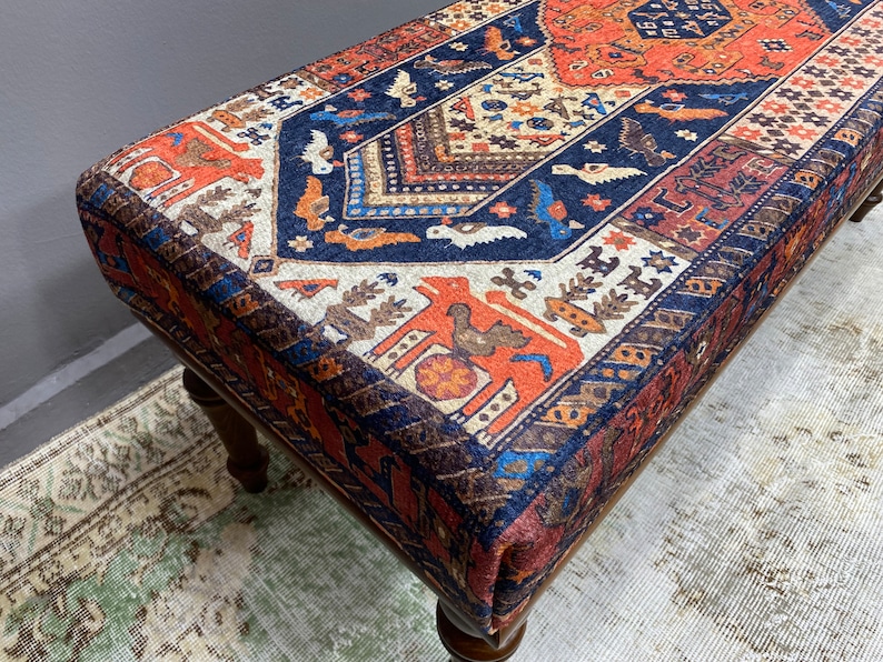 May include: A wooden bench with a colourful patterned cushion. The cushion features a geometric design with red, blue, and white colours. The bench is made of dark wood and has a traditional style.