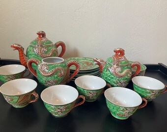 May include: A green and red dragon tea set with a teapot, creamer, sugar bowl, and six cups. The set is decorated with gold accents and dragon designs.
