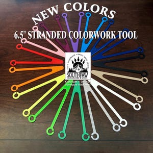 May include: A variety of 6.5 inch stranded colorwork tools in different colors, arranged in a circle on a wooden surface. The tools are made by Southpaw Fiber Arts.