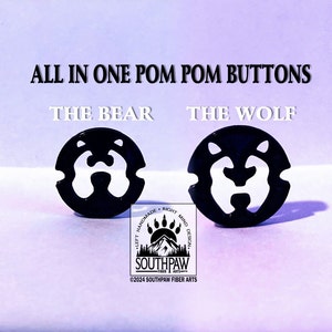 May include: Two black pom pom buttons, one with a bear face and the other with a wolf face. The buttons are on a purple background with the text "All in one pom pom buttons" and "The Bear" and "The Wolf" above them. The text "Left Handmade Right Mind Design" and "Southpaw Fiber Arts" is below the buttons.