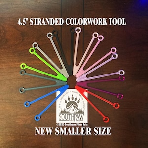May include: A set of 12 colorful 4.5 inch stranded colorwork tools arranged in a circle on a wooden surface. The tools are made of plastic and have a loop at each end. The text "4.5" STRANDED COLORWORK TOOL" is at the top of the image. The text "NEW SMALLER SIZE" is at the bottom of the image. The text "LEFT HANDMADE RIGHT MIND DESIGN" and "SOUTHPAW FIBER ARTS" is in the center of the image.