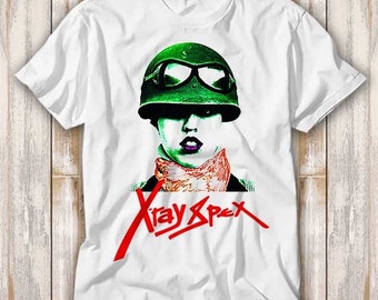 May include: White t-shirt with a green and black illustration of a person wearing a helmet and goggles. The text "X-Ray Spex" is printed in red on the shirt.