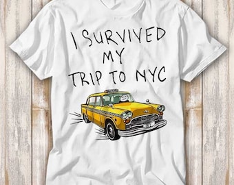May include: White t-shirt with the text "I survived my trip to NYC" in black. A yellow taxi cab is illustrated below the text.