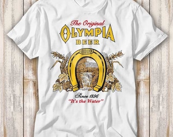 May include: White t-shirt with a yellow and red graphic of the Olympia Beer logo. The logo features a horseshoe with a waterfall and the text "The Original Olympia Beer, Good Luck, Since 1896, "It's the Water."