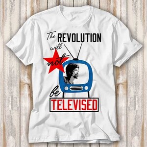 May include: White t-shirt featuring a blue and white television graphic and a red star. The text on the shirt reads "The Revolution will not be Televised".