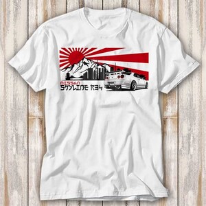 May include: White t-shirt with a graphic of a white Nissan Skyline R34 car in front of a red and white Japanese flag with a rising sun and a mountain range in the background. The text "NISSAN SKYLINE R34" is printed below the car.