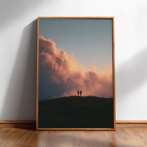 a framed photograph of two people standing on a hill, with a dramatic sky in the background.