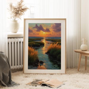 a large framed painting of a serene landscape with a river, grass, and a sunset sky. The painting is displayed on a white wall in a cozy living room setting, with a window, a radiator, and a vase of flowers nearby.