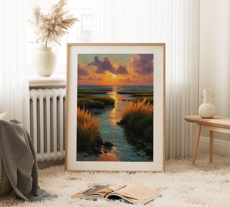 a large framed painting of a serene landscape with a river, grass, and a sunset sky. The painting is displayed on a white wall in a cozy living room setting, with a window, a radiator, and a vase of flowers nearby.