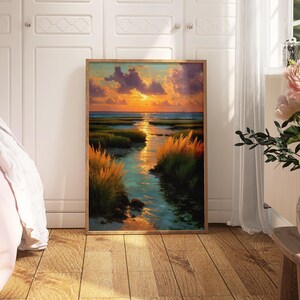 a large framed painting of a serene landscape with a river, grass, and a sunset sky, displayed in a room with white walls and a wooden floor.