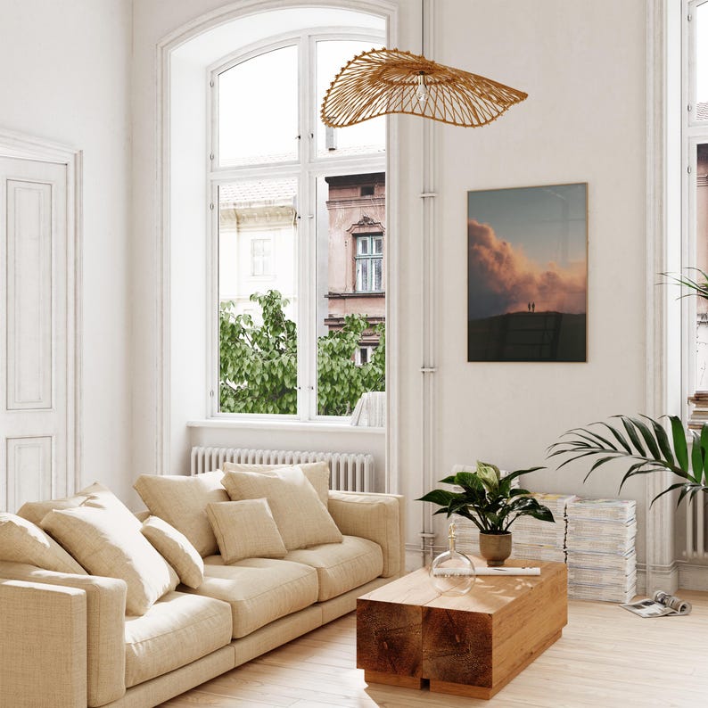 A bright and airy living room with a large window, a beige sofa, a wooden coffee table, and a hanging woven light fixture.