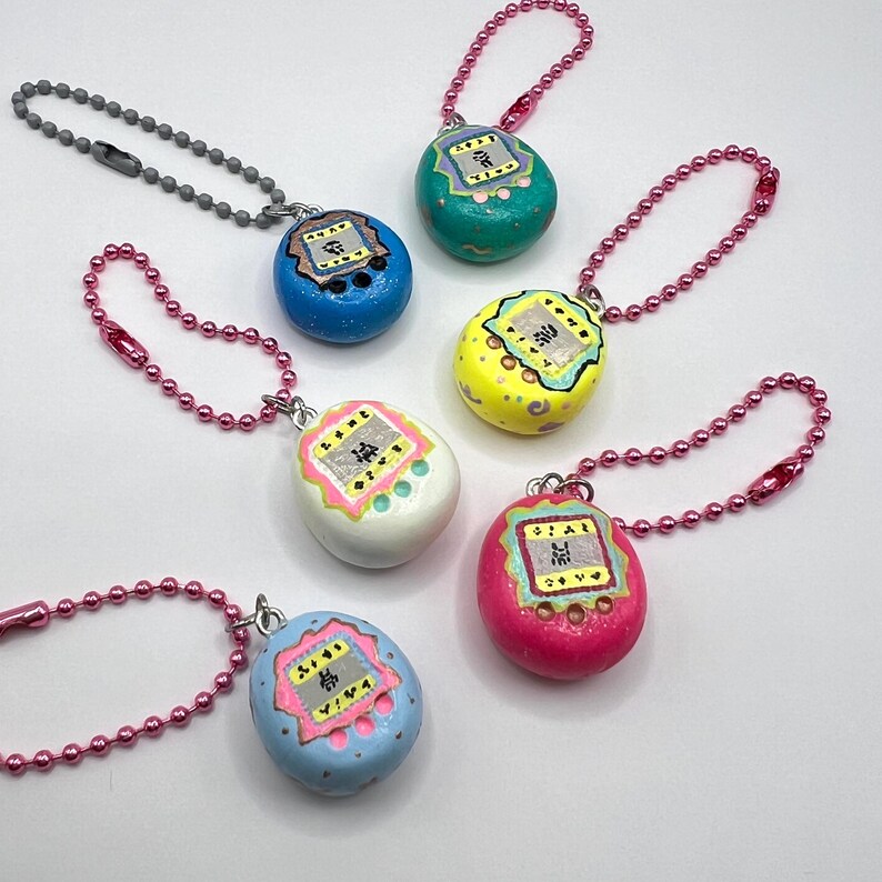 Puede incluir: Una colecci&oacute;n de seis llaveros coloridos en forma de huevo. Cada llavero presenta un color diferente, incluyendo azul, verde, amarillo, blanco y rosa. Tienen un peque&ntilde;o dise&ntilde;o similar a una pantalla con caracteres japoneses y est&aacute;n unidos a una cadena.
