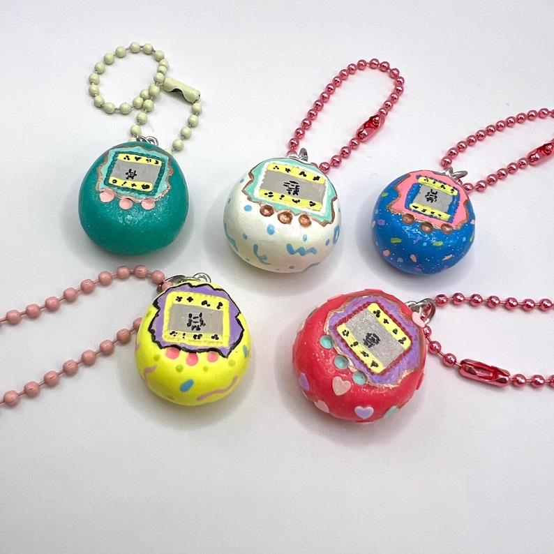 Puede incluir: Cinco colgantes coloridos, pintados a mano, con forma de huevo, con peque&ntilde;as pantallas y cadenas de bolas. Los colgantes son de color turquesa, blanco, azul, amarillo y rojo, cada uno con dise&ntilde;os &uacute;nicos. Recuerdan a los juegos port&aacute;tiles retro.