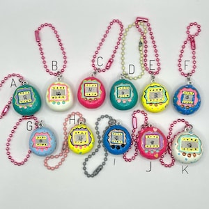 Puede incluir: Una colecci&oacute;n de once llaveros coloridos en forma de huevo. Cada llavero presenta un dise&ntilde;o pintado con una peque&ntilde;a pantalla y caracteres japoneses. Los llaveros est&aacute;n sujetos a cadenas de bolas rosas o plateadas. Los colores incluyen turquesa, blanco, rosa, verde, amarillo, azul y azul claro.