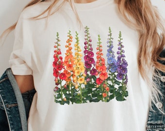 May include: A white t-shirt with a rainbow floral design. The flowers are arranged in a vertical line and are in the colors of the rainbow. The flowers are a type of snapdragon.