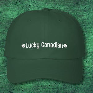 May include: A dark green baseball cap featuring the text "Lucky Canadian" in white, with white shamrock motifs. The cap has a curved peak and an adjustable fabric strap.