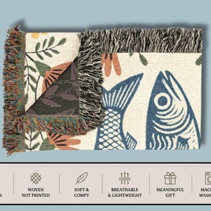 May include: Woven cotton throw blanket with a fish and floral design. The blanket features a cream background with blue fish and orange and green floral accents. The edges have a fringed trim. The blanket is machine washable.