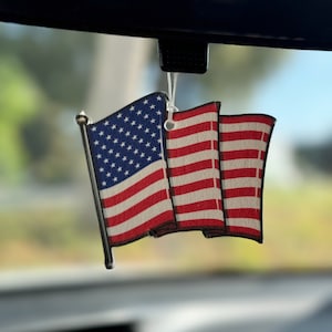 May include: A red, white and blue American flag car air freshener hanging from a rear view mirror.