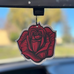 May include: A red rose car air freshener hanging from a rearview mirror. The rose is drawn in a cartoon style with a white background.
