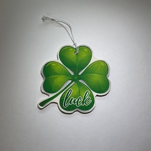 May include: A green four-leaf clover car air freshener with the word "luck" written in white cursive.