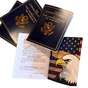 May include: Several copies of "The Constitution of The United States of America" in navy blue with gold lettering and an eagle emblem. An open booklet displays the text of the amendments and a patriotic eagle illustration.