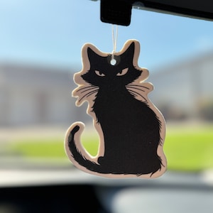 May include: A black cat silhouette car air freshener hanging from a rearview mirror. The cat is sitting with its tail curled around its legs.