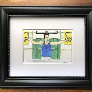 May include: A framed cartoon drawing of a man holding onto two rings. The man is wearing a blue tank top and is in a gym setting. The text on the drawing reads "I'm still holding, still holding."