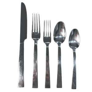 Puede incluir: Un juego de cinco piezas de cubertería de acero inoxidable, que incluye un cuchillo, dos tenedores y dos cucharas. Los utensilios tienen un diseño sencillo y moderno con un acabado pulido, dispuestos sobre un fondo blanco. Ideal para comidas diarias u ocasiones especiales.