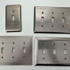 May include: Four brushed nickel light switch plates with varying numbers of switches. The plates have a rectangular shape and a smooth, metallic finish.