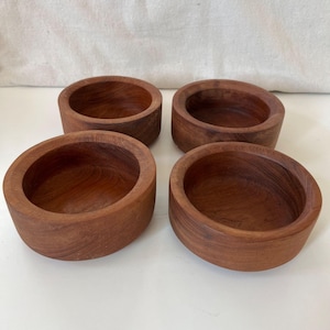 Könnte beinhalten: Vier kleine, runde Holzschalen in einem satten, rötlich-braunen Farbton. Die Schalen haben eine glatte, polierte Oberfläche und ein schlichtes Design. Sie dienen wahrscheinlich zum Servieren von Snacks oder kleinen Portionen. Jede Schale hat einen Durchmesser von ca. 10 cm.