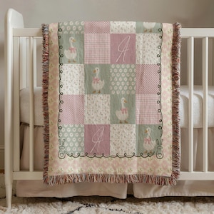 May include: A patchwork baby blanket with a charming design. The blanket features squares of pink, green, and white fabrics, some with floral patterns, gingham, and a repeating goose motif. The blanket is fringed and has the letter "A" embroidered on it.