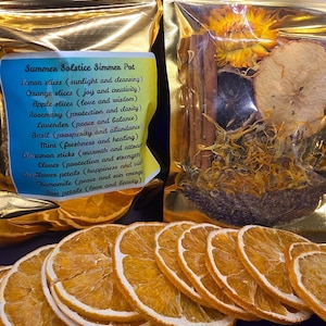 May include: A gold pouch filled with dried fruit, herbs, and spices. The pouch is labeled "Summer Solstice Simmer Pot" and lists the ingredients: lemon slices, orange slices, apple slices, rosemary, lavender, basil, mint, cinnamon sticks, cloves, sunflower petals, chamomile, and rose petals.