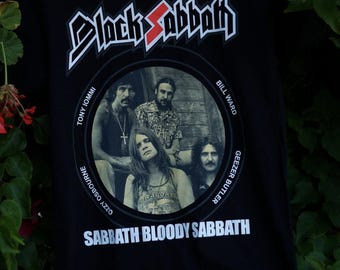 May include: Black Sabbath band t-shirt with a black and white photo of the band members in a circle. The band members are Tony Iommi, Ozzy Osbourne, Geezer Butler, and Bill Ward. The text "Black Sabbath" is in a large, bold font above the photo. The text "Sabbath Bloody Sabbath" is below the photo.
